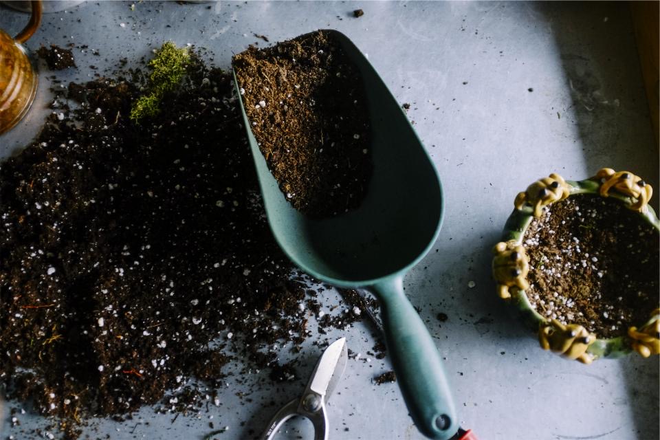 Trowel scooping potting soil beside small plant pots